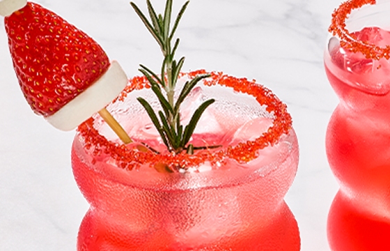 Two cosmo cocktails in bubble glasses, garnished with a red sugar rim and strawberry santa hat.
