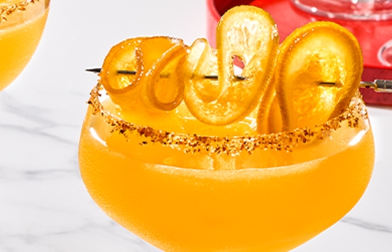 Two Mandarita cocktails garnished with a tajin rim and curled orange peel.